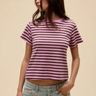 Person wearing a pink and purple striped t-shirt with light blue jeans on a beige background