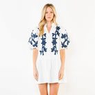 Woman wearing a white dress with blue floral patterns on a plain background
