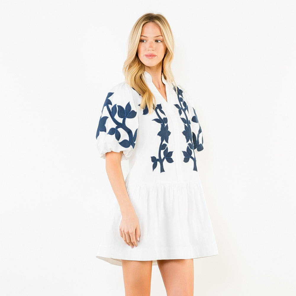Woman wearing a white dress with blue floral patterns on a plain background