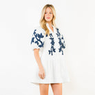 Woman wearing a white dress with blue floral patterns on a plain background