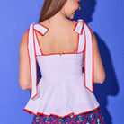 Woman wearing a white top with red trim and blue shorts with floral pattern against a blue background